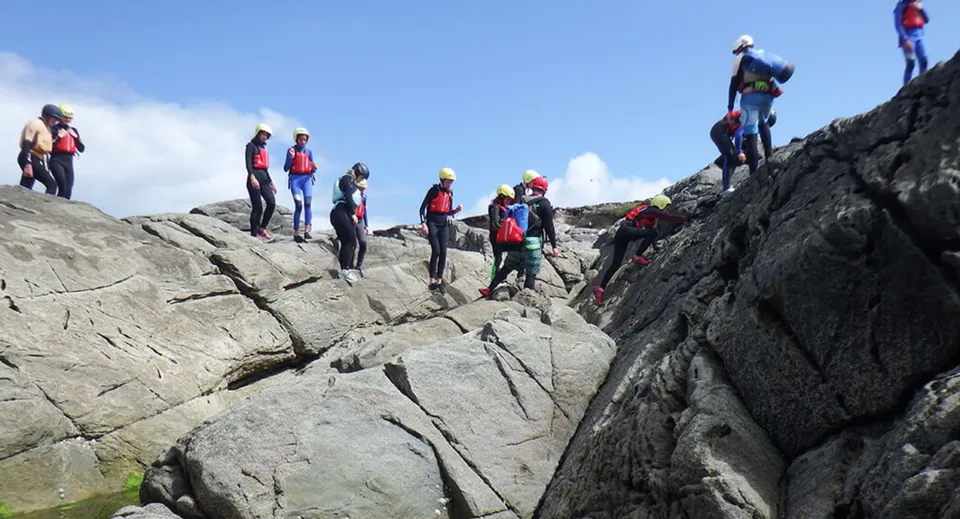 Studenti della Carrick on Shannon Community School si arrampicano con attrezzatura colorata su un terreno roccioso sotto un cielo limpido.