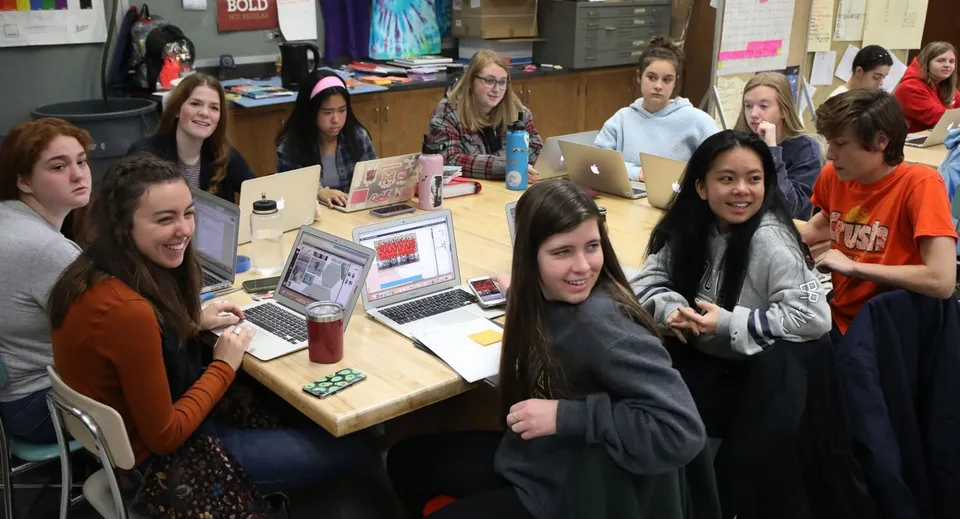Un gruppo di studenti del Don College lavora insieme con i laptop a un tavolo in classe.