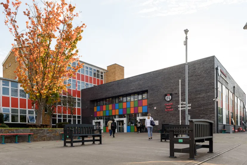 L'edificio colorato e moderno della Cardiff High School con un albero autunnale in primo piano e persone all'interno del campus scolastico.