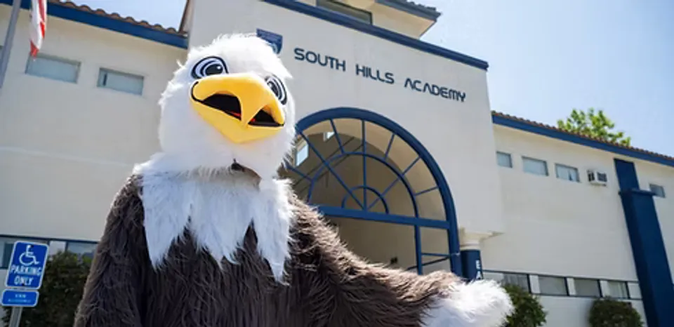 La mascota águila de la South Hills Academy posa delante del edificio escolar con el rótulo del colegio.