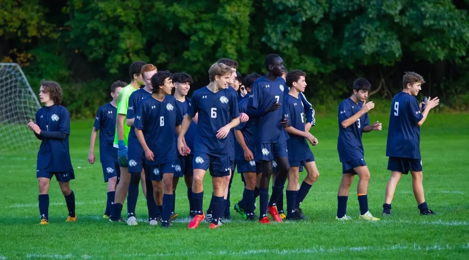 Un gruppo di giovani calciatrici e calciatori in maglia blu si trova sul campo sportivo della Allendale Columbia School.