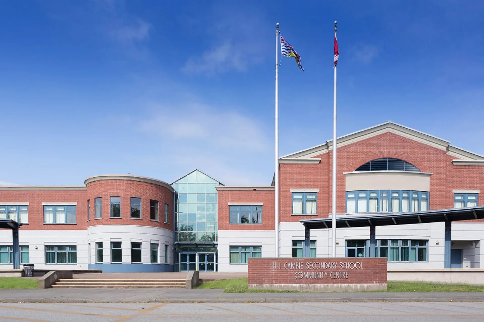 L'edificio moderno a più piani in mattoni della H.J. Cambie Secondary School con ingresso in vetro e bandiere davanti al cielo blu.