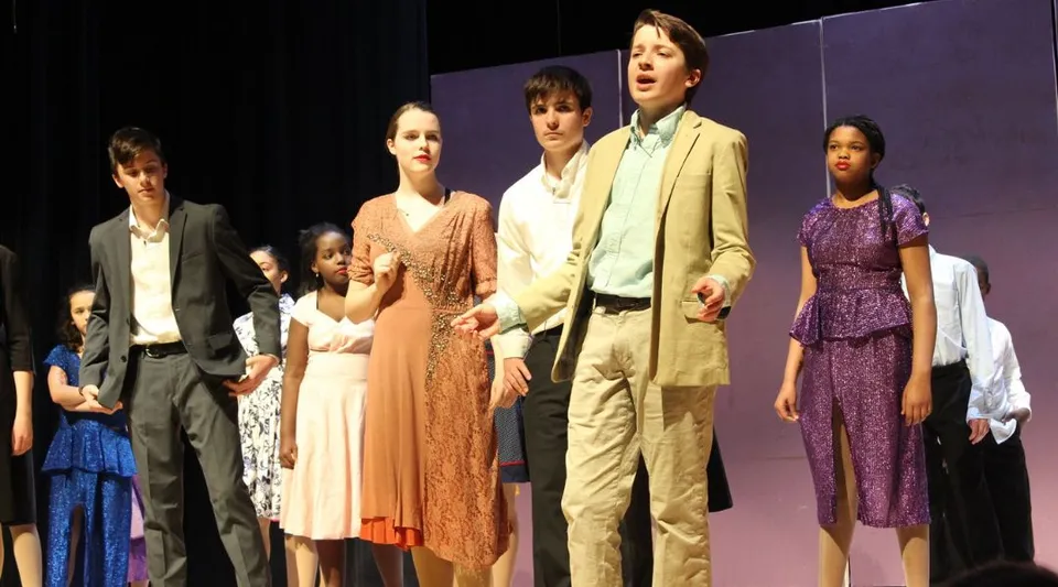 Un gruppo di studenti della Friends School of Baltimore si trova in abiti formali su un palco con sfondo viola.