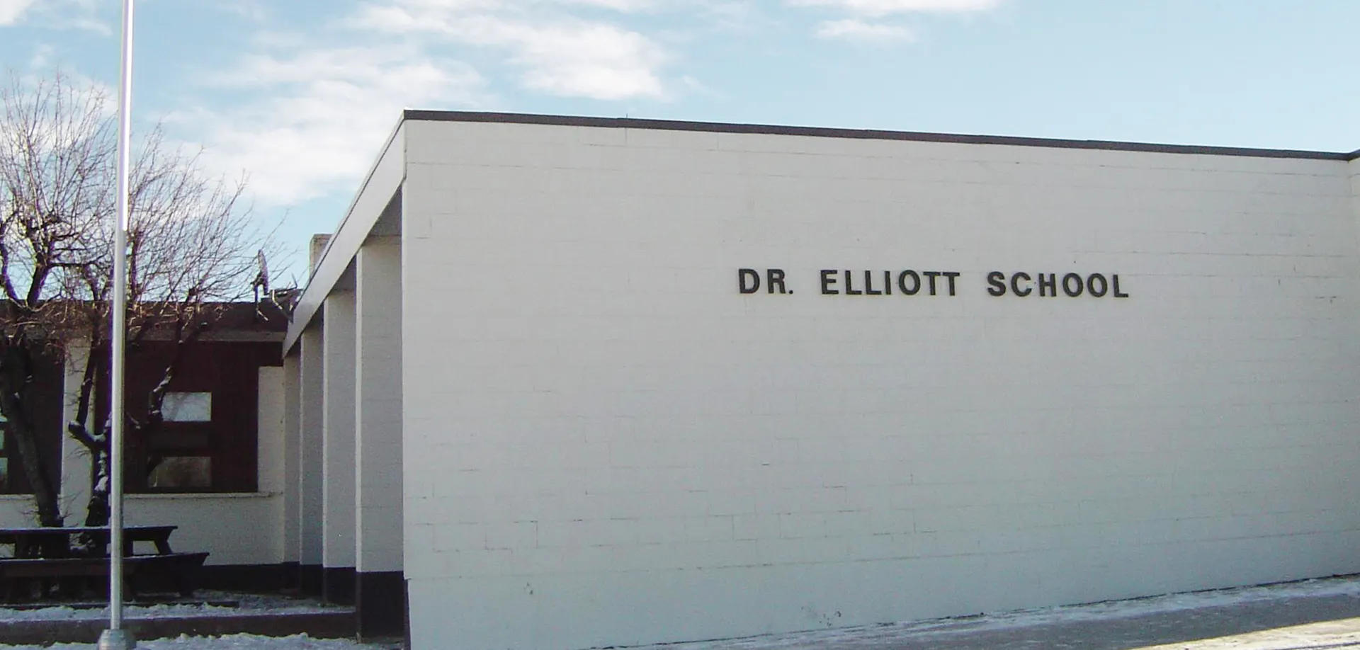 L'edificio scolastico moderno della Dr. Elliott School con la scritta ben visibile sotto un cielo nuvoloso.