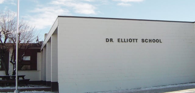 L'edificio scolastico moderno della Dr. Elliott School con la scritta ben visibile sotto un cielo nuvoloso.