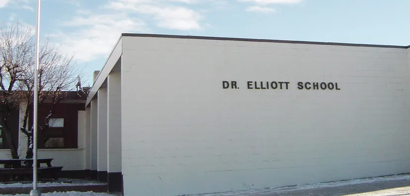 L'edificio scolastico moderno della Dr. Elliott School con la scritta ben visibile sotto un cielo nuvoloso.