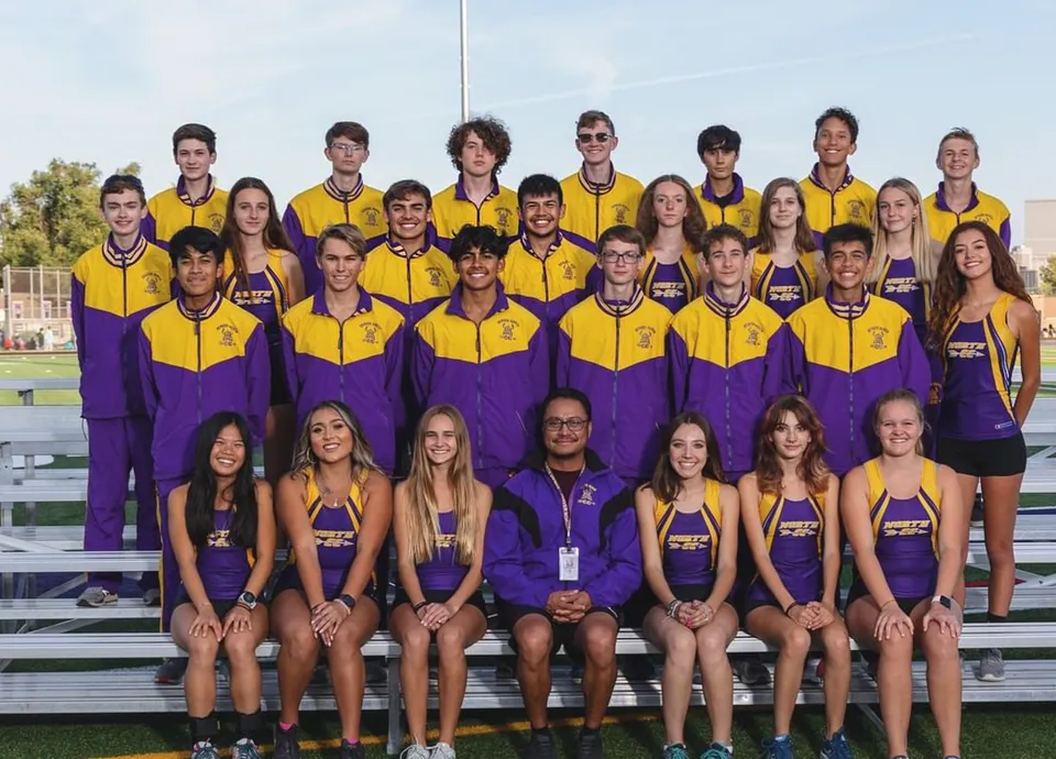 Un gruppo di giovani atleti in divisa giallo-viola posa sul campo sportivo del Denver Public School District con uno stadio sullo sfondo.