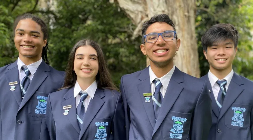 Quattro studenti della Hunters Hill High School sono insieme in un ambiente naturale con alberi sullo sfondo.