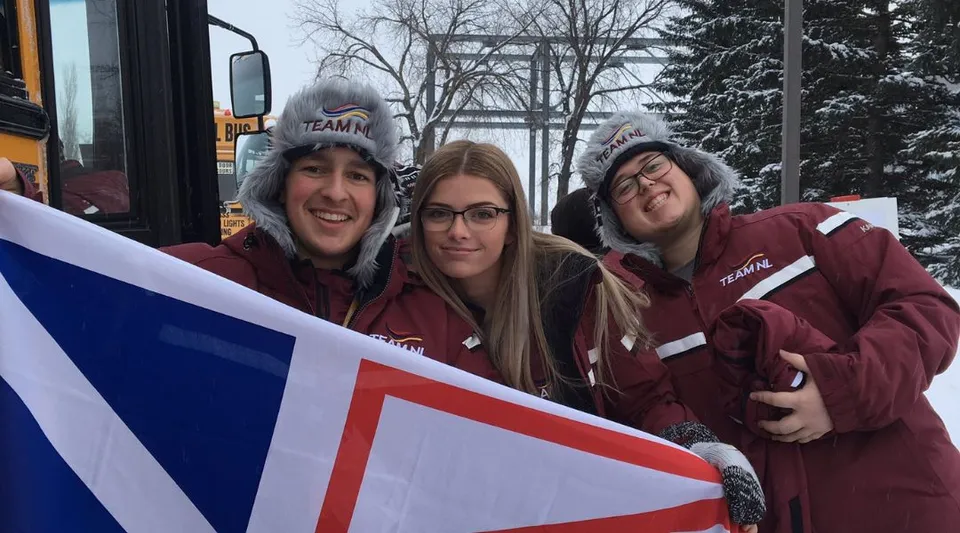 Tre studentesse del Dorset Collegiate indossano felpe con cappuccio rosse identiche e tengono insieme un grande striscione.