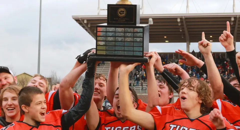 Un gruppo di studenti delle Tacoma Public Schools festeggia la vittoria di un trofeo davanti a un edificio simile a uno stadio.