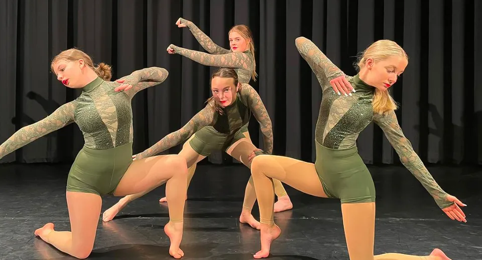 Studentesse della Ipswich High School eseguono un'esibizione di danza sincronizzata su un palco con uno sfondo nero.