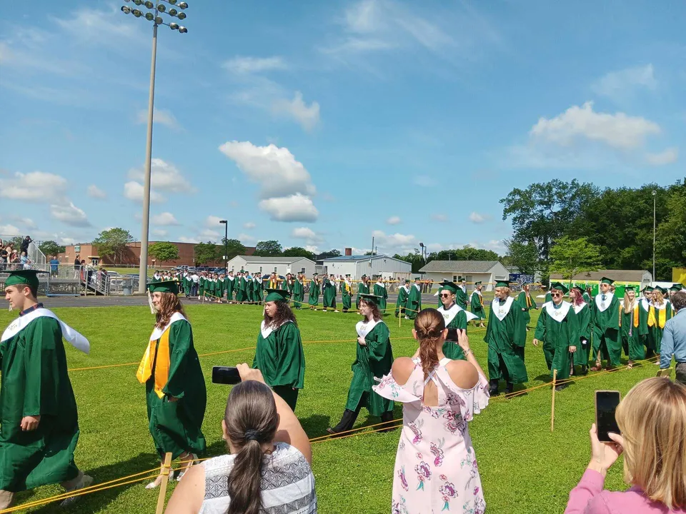 I diplomati della Coventry High School in toga verde e gialla si trovano su un prato davanti a un edificio in mattoni.
