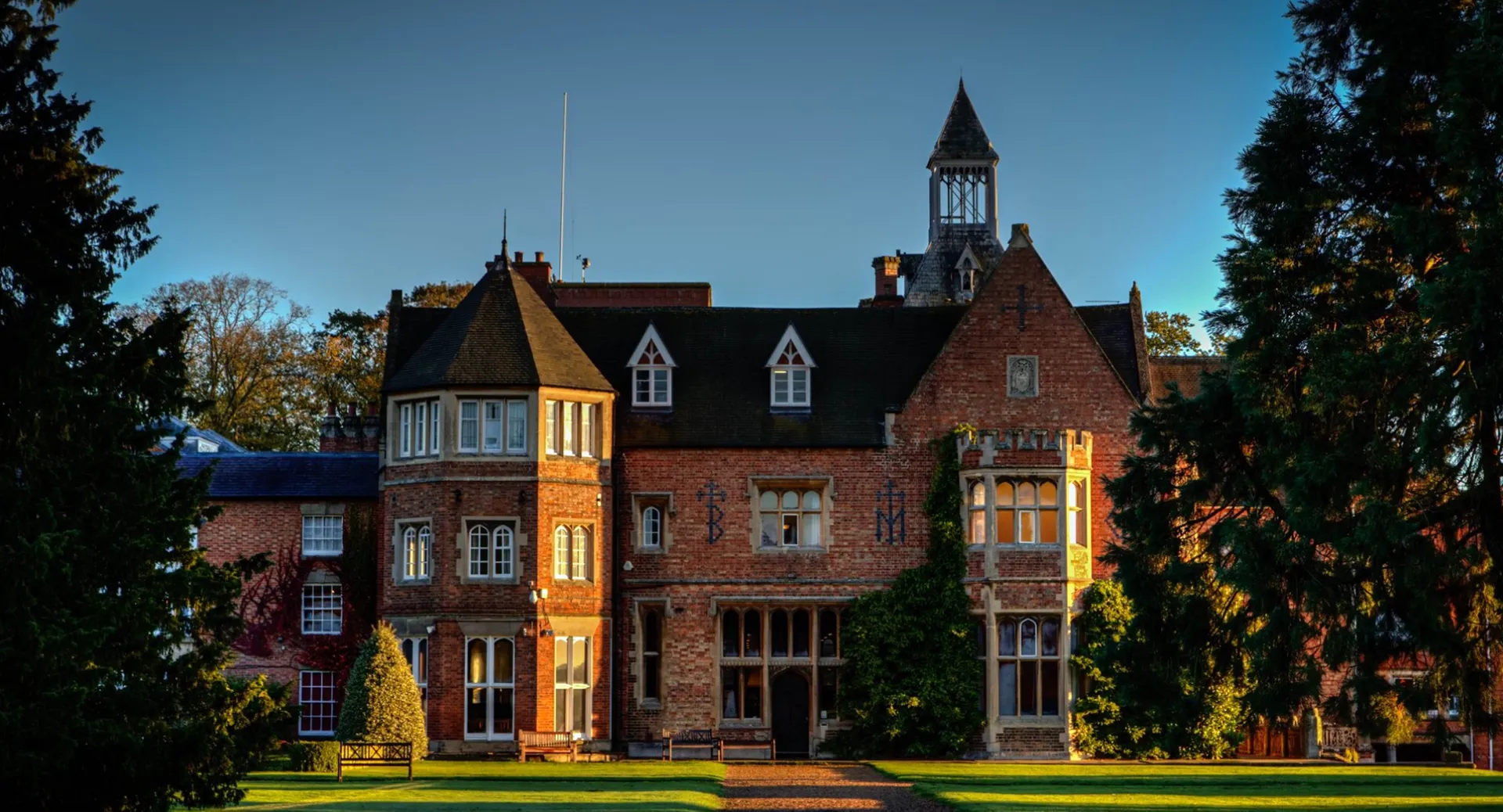 L'edificio storico in mattoni della Rugby School è circondato da prati e alberi sotto un cielo azzurro e limpido.