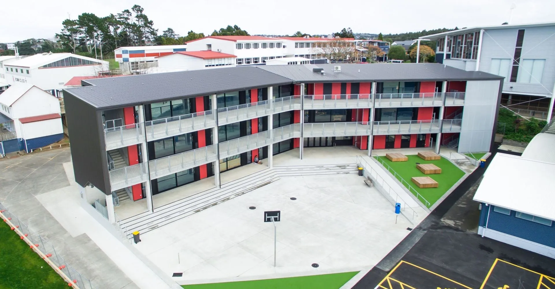L'edificio moderno a più piani del Rosmini College, con un design nei colori rosso e bianco, è circondato da altri edifici e da un prato.