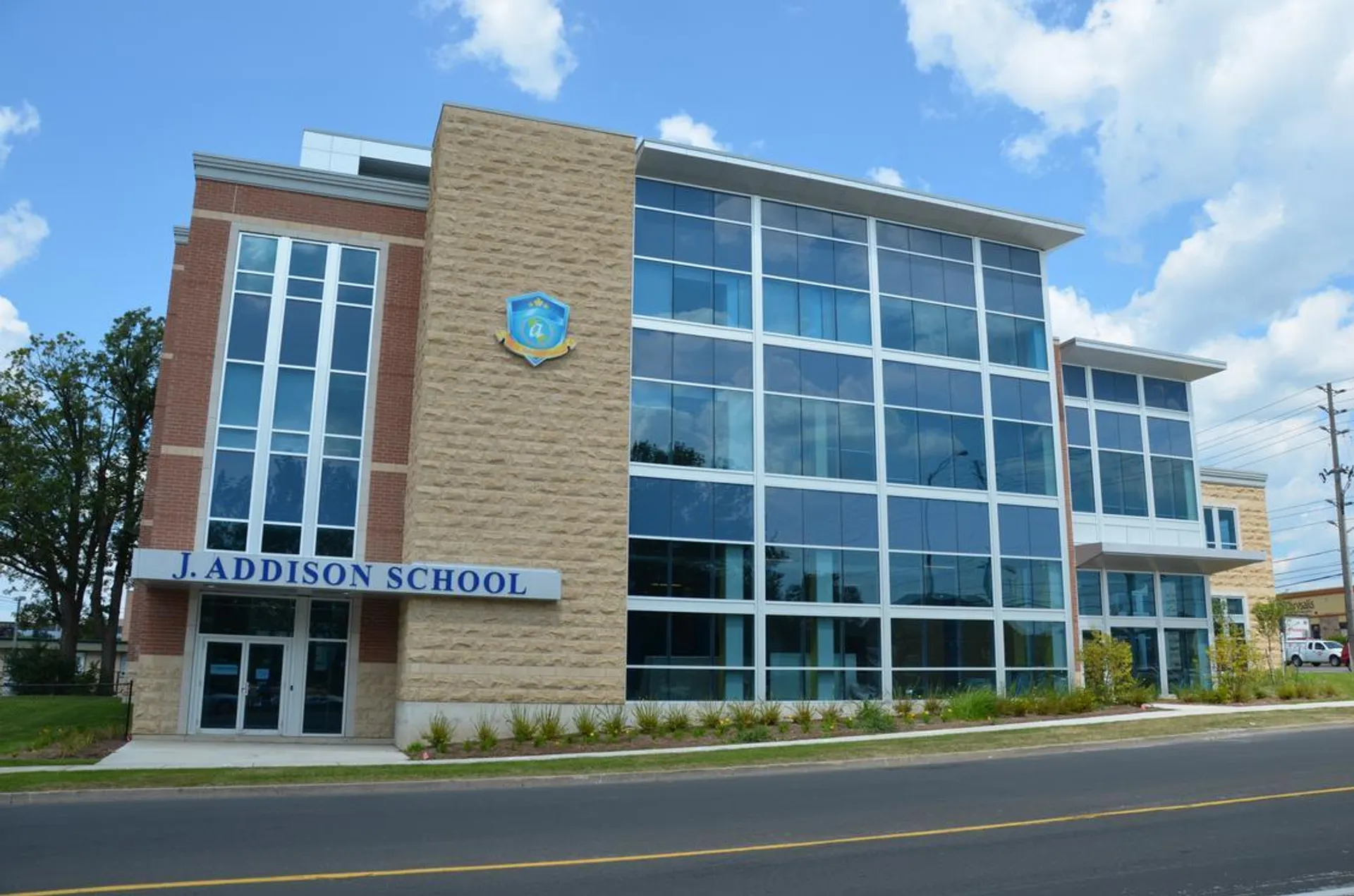 L'edificio scolastico moderno della J. Addison School, con ampie vetrate, si trova in un ambiente simile a un parco.