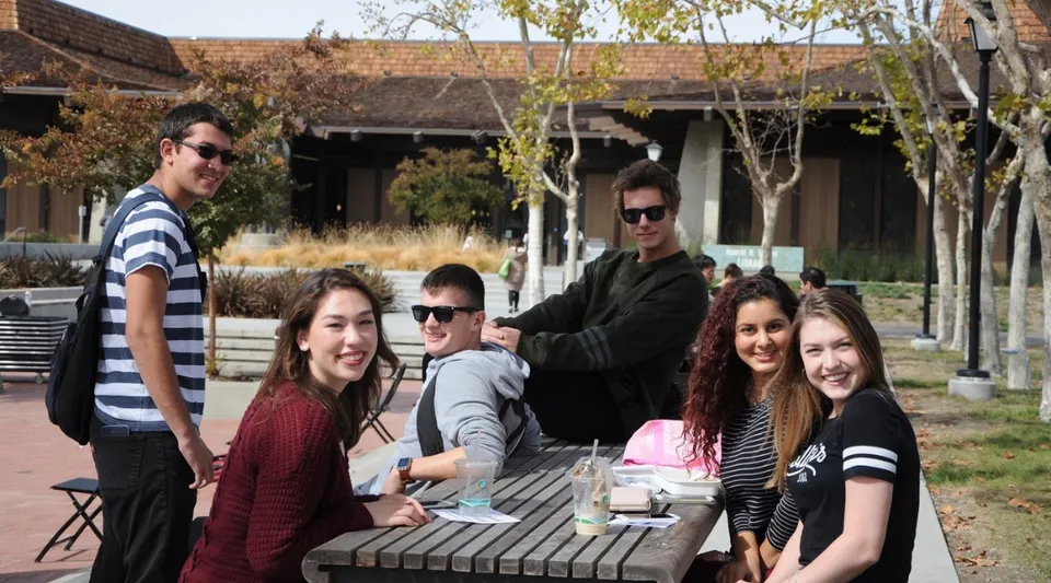 Un gruppo di studenti si raduna su una terrazza in legno davanti a un edificio rustico nel campus del Foothill College.