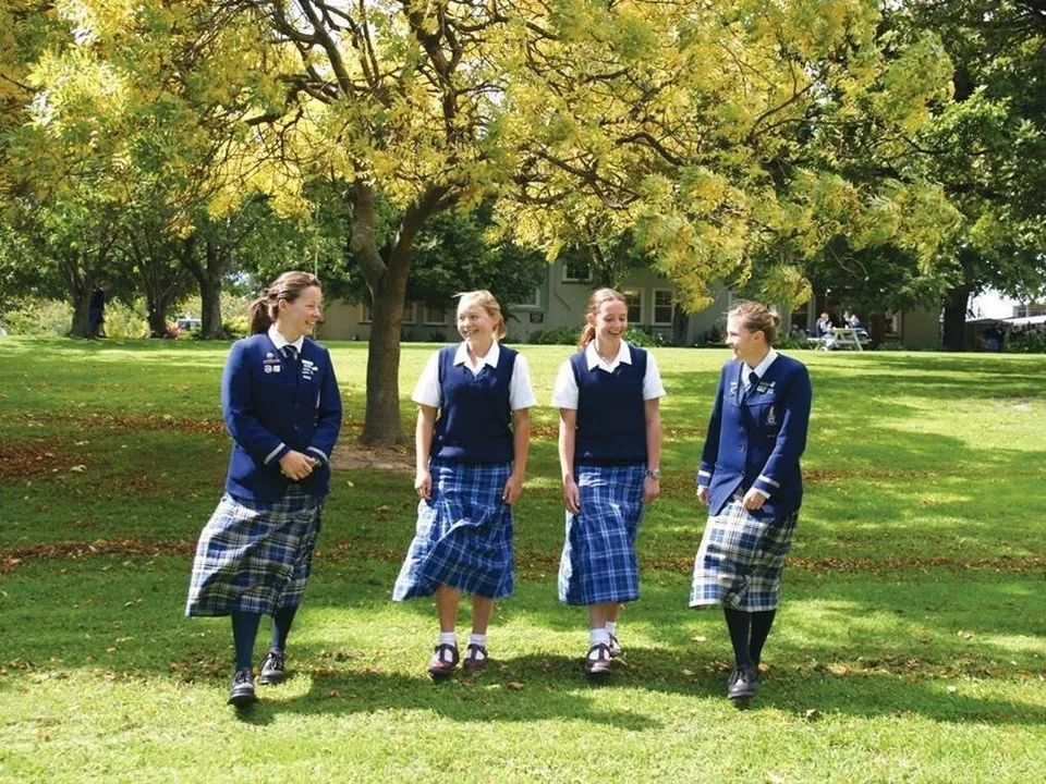 Quattro studentesse della Timaru Girls School sono in piedi su un prato in un parco con alberi sullo sfondo.