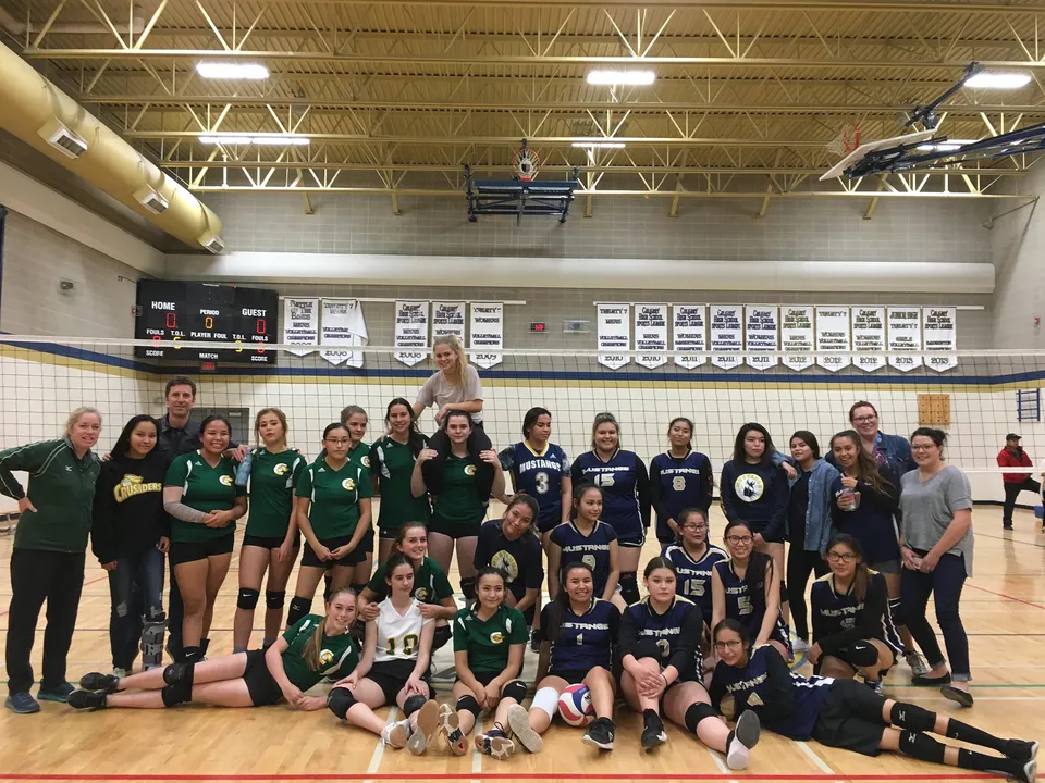 Un gruppo di studentesse della Canmore Collegiate High School posa in abbigliamento sportivo in palestra davanti ad attrezzi sportivi e striscioni.