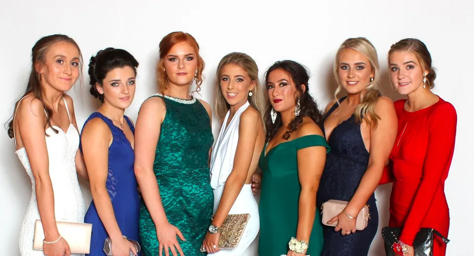 Sei studentesse della Royal School Dungannon posano in abiti colorati davanti a uno sfondo bianco.