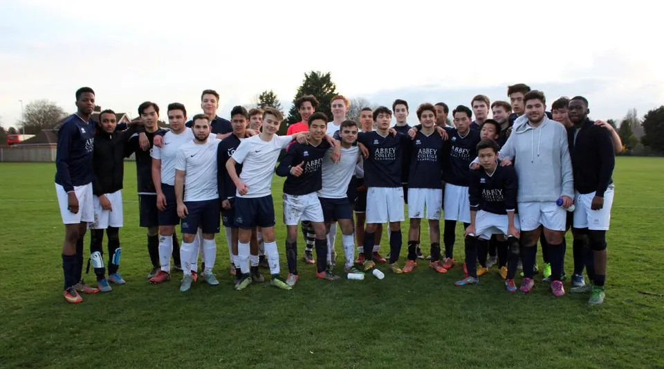 Un gruppo di studenti dell'Abbey College di Cambridge si trova insieme su un campo da calcio sotto un cielo nuvoloso.
