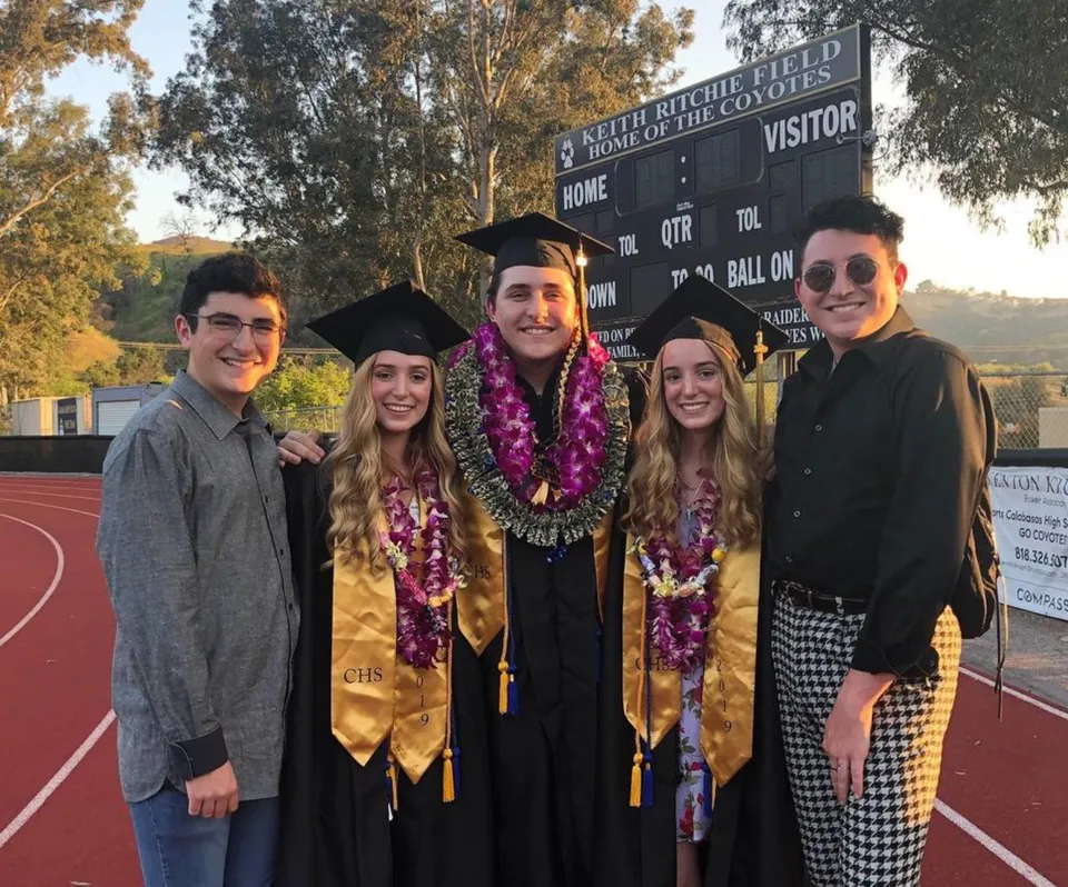 Un gruppo di diplomati in abito accademico sta in piedi davanti a un logo nel campus della Calabasas High School.