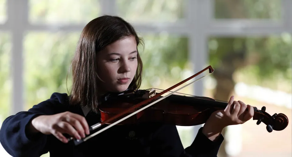 Una studentessa della Archbishop's School suona concentrata il violino davanti a uno sfondo naturale sfocato.