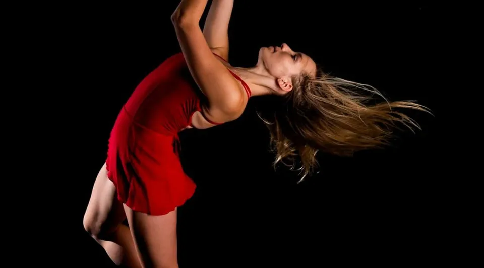 Una donna in maglia rossa balla su uno sfondo scuro nel campus del Coffs Harbour Senior College.