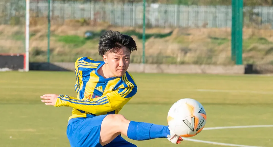 Uno studente della MPW Birmingham gioca a rugby su un campo d'erba circondato da una recinzione metallica.