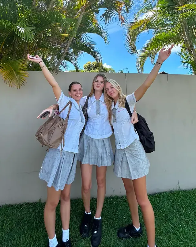 Tre studentesse in divisa scolastica alzano le braccia sorridenti tra le palme durante un anno all'estero in Australia