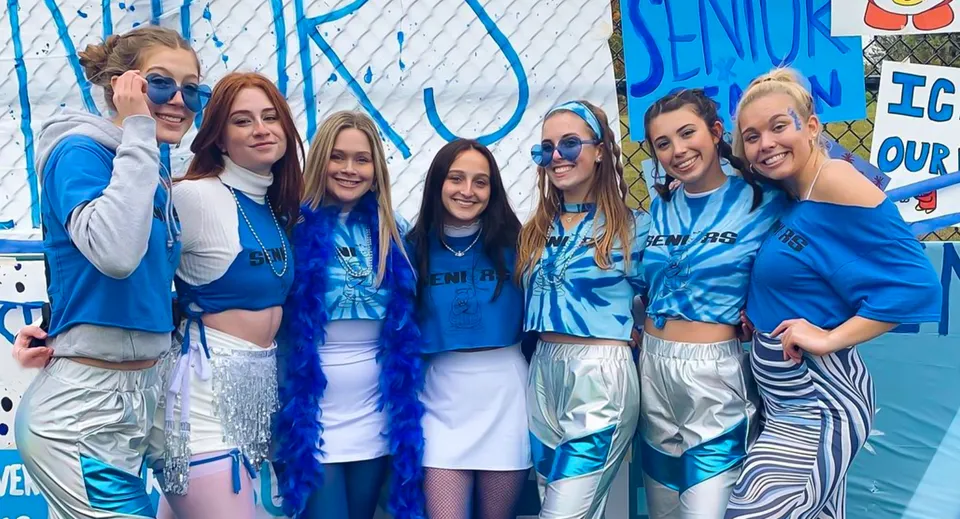Sette studentesse della Mercyhurst Prep School in posa con abiti blu e bianchi davanti a un manifesto.