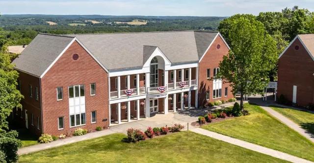 L'edificio in mattoni a più piani della Woodstock Academy si erge davanti a colline verdi e circondato da una lussureggiante vegetazione.