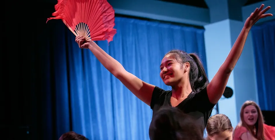 Una donna in abito nero tiene un ventaglio rosso e si esibisce sul palco della British International School Houston.