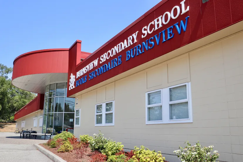 Il grande edificio rosso della Burnsview Secondary School si erge sotto un cielo azzurro e limpido, circondato da aree verdi.