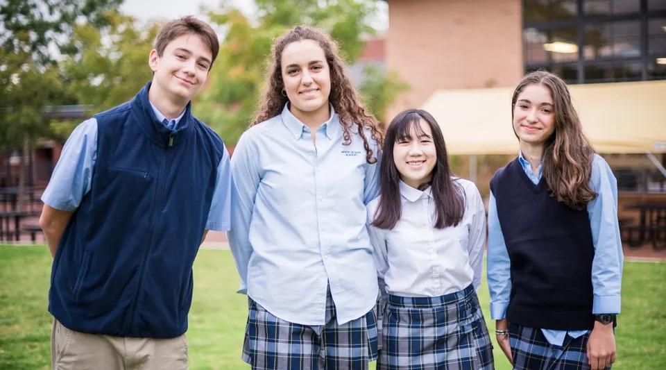 Un gruppo di quattro studenti si trova nell'area esterna della Mount De Sales Academy con alberi ed edifici sullo sfondo.
