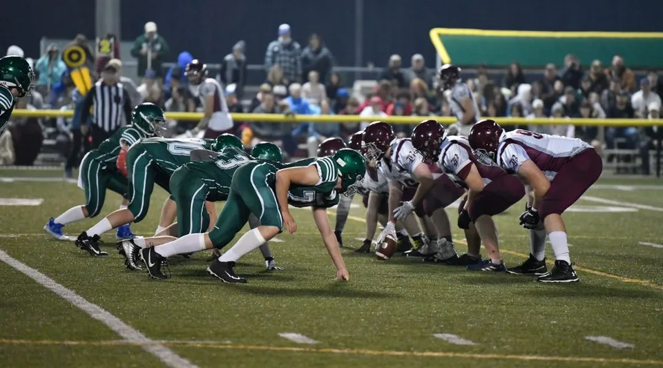 Giocatori di football americano della West Ferris School si schierano in campo durante una partita in notturna.