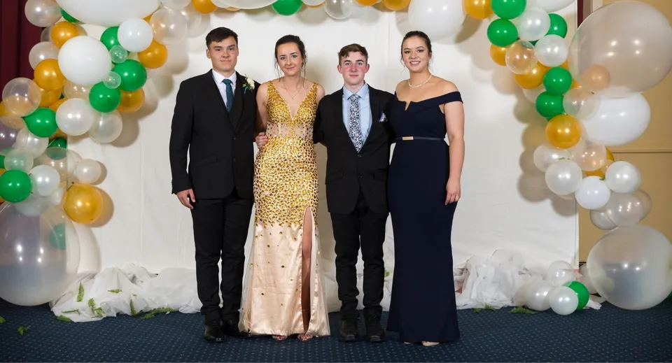Quattro persone posano davanti a palloncini colorati e fiori nel campus della Dannevirke High School.
