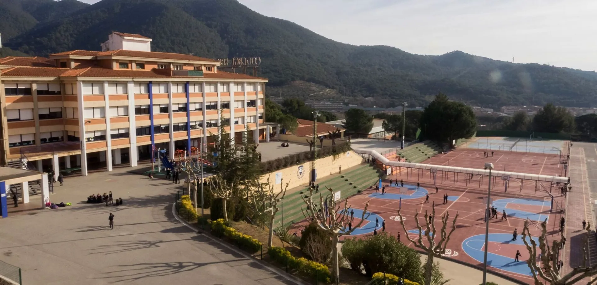L'edificio a più piani della SEK International School Catalunya con facciata colorata è circondato da aree verdi e montagne.