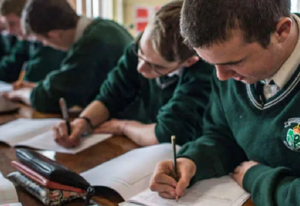 Studenti in divisa scolastica siedono concentrati ai loro banchi durante le lezioni alla Coláiste Chríost Rí.