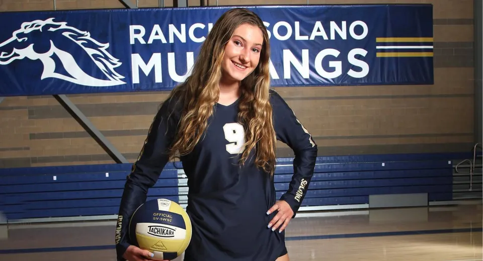 Una studentessa della Rancho Solano Preparatory School sta davanti a uno striscione dei Mustangs con in mano un pallone da pallavolo.