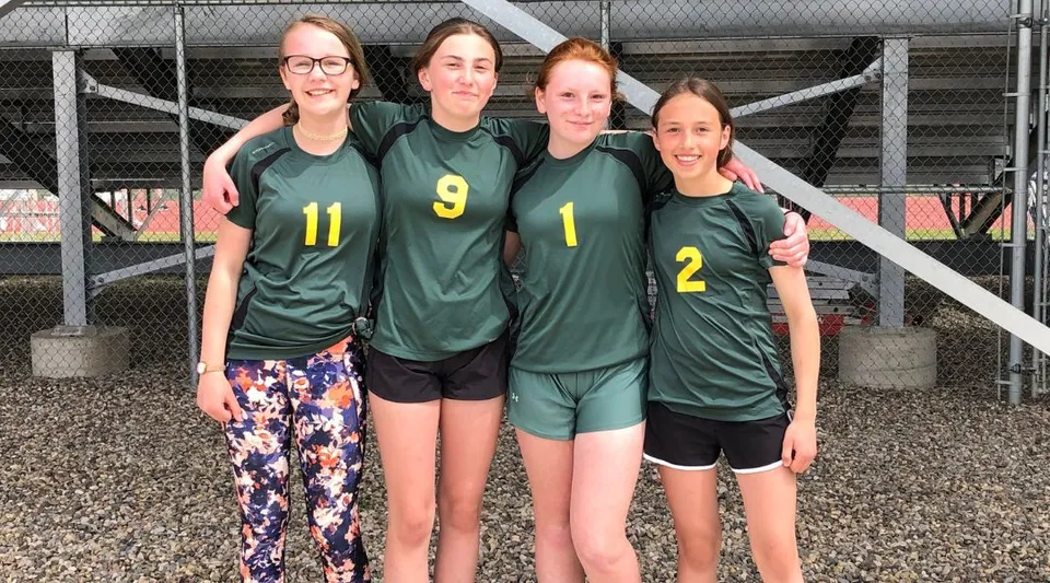 Quattro studentesse della Noble Central School sono insieme in maglie sportive verdi davanti a una recinzione in rete metallica.