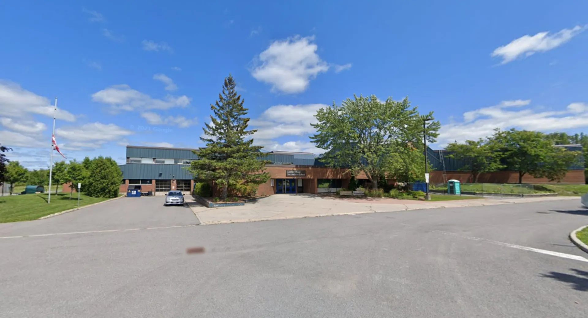 L'edificio moderno a più piani della Cairine Wilson Secondary School con un grande parcheggio e circondato da alberi sotto un cielo blu.