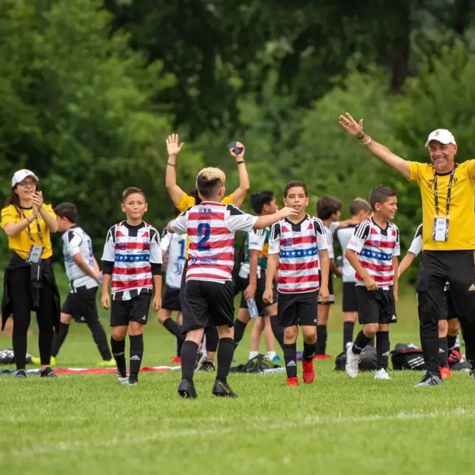 Giovani calciatori della Van Houston Academy e i loro allenatori festeggiano su un campo da calcio.