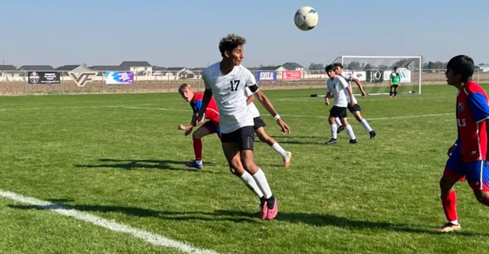 Un giocatore di calcio della American Falls High School salta verso il pallone durante una partita sul campo in erba.