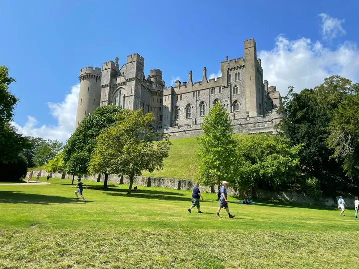Arundel Castle mit Türmen und Zinnen über einer grünen Wiese mit Spaziergängern