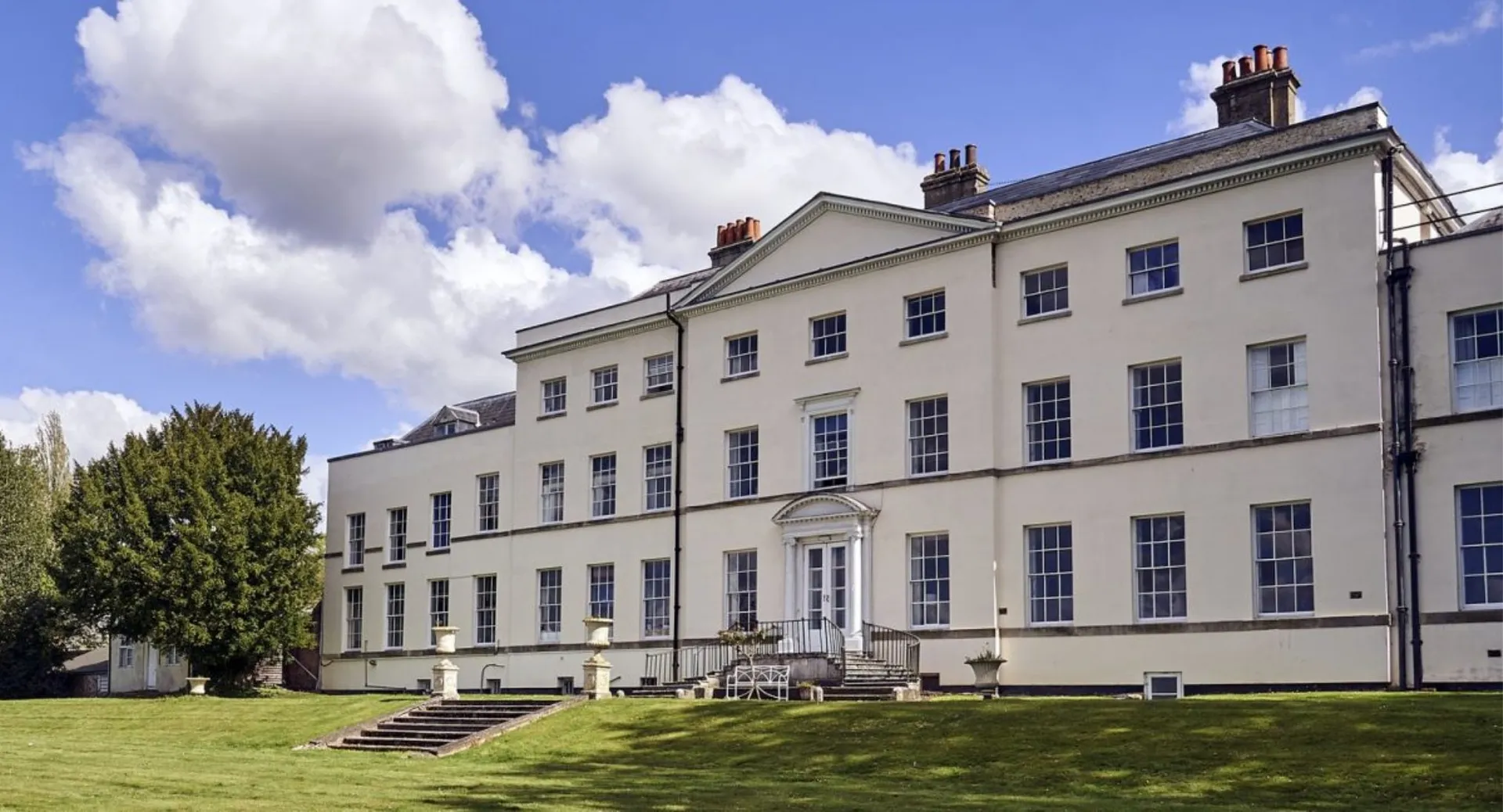 El edificio principal de varios pisos de Padworth College está rodeado de césped bien cuidado y vegetación verde bajo un cielo nublado.