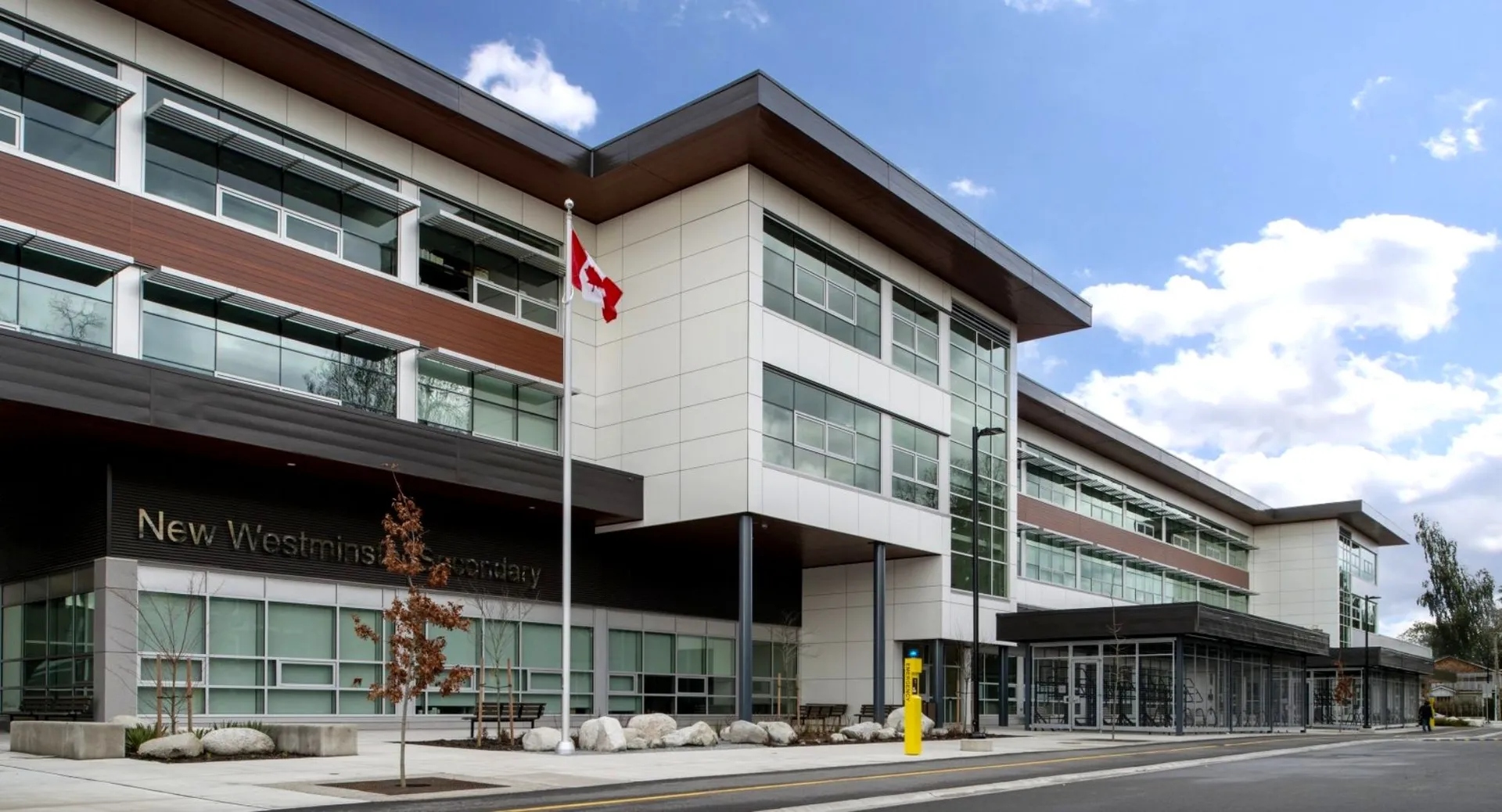 L'edificio moderno a più piani della Westminster Secondary School con facciata in vetro e bandiera canadese sotto un cielo nuvoloso.
