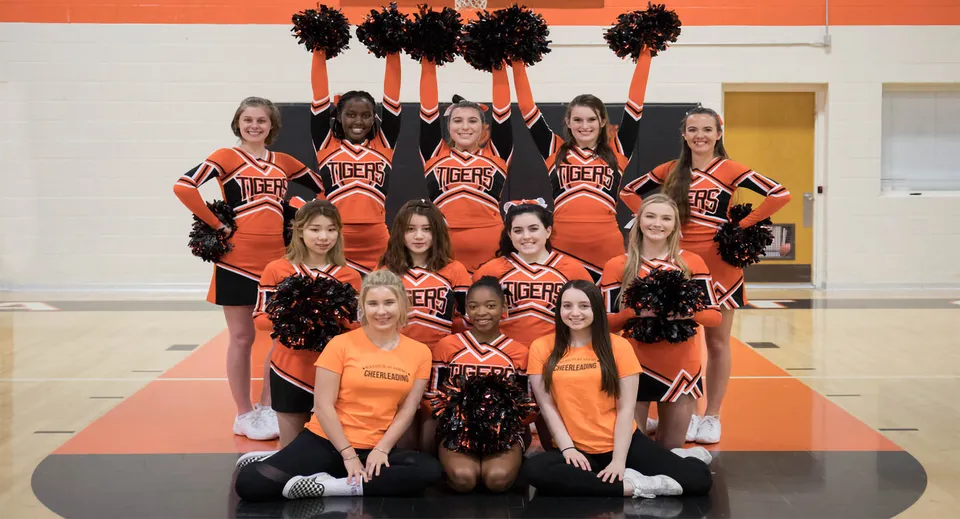 Un gruppo di cheerleader della Wasatch Academy in posa con uniformi arancioni e nere in palestra.