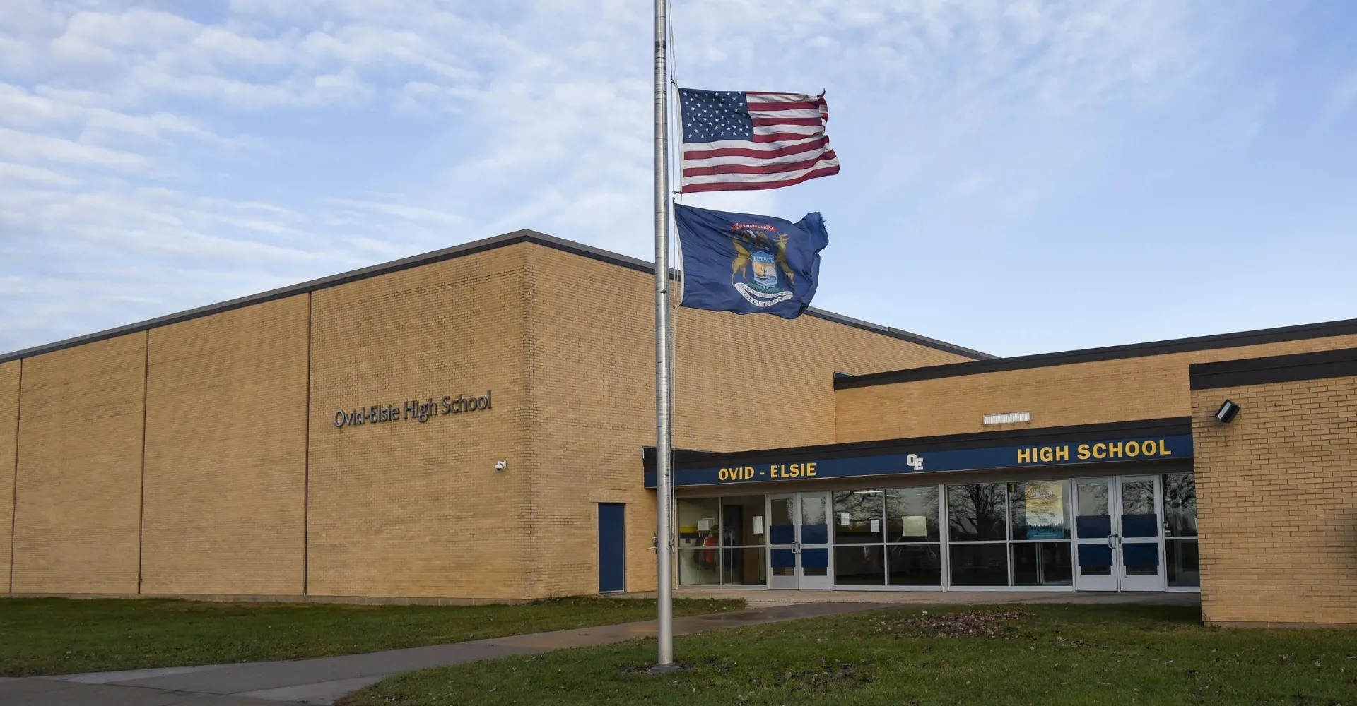 L'edificio della Ovid-Elsie High School con la bandiera americana e quella dello Stato su un pennone in primo piano.