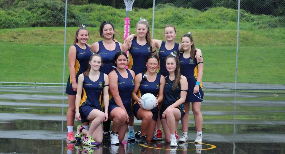Un gruppo di giovani atlete dell'Upper Hutt College in posa su un campo erboso con un campo sportivo e alberi sullo sfondo.