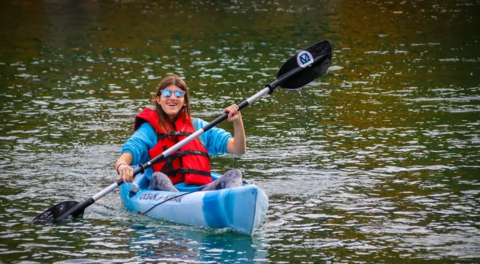Una persona con un giubbotto di salvataggio rosso pagaia su un kayak blu nell'acqua all'interno del campus della The Village School.